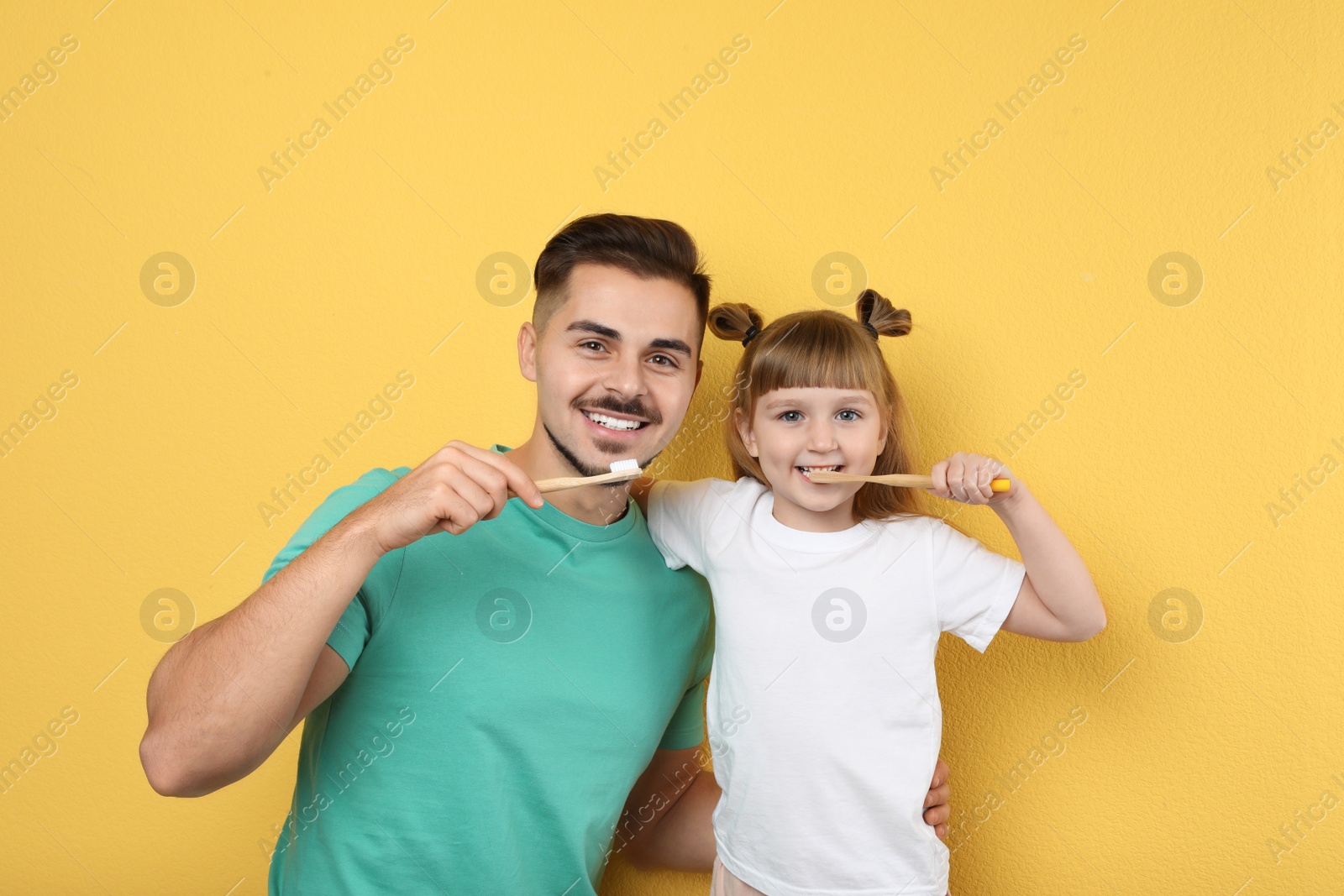 Photo of Little girl and her father brushing teeth together on color background