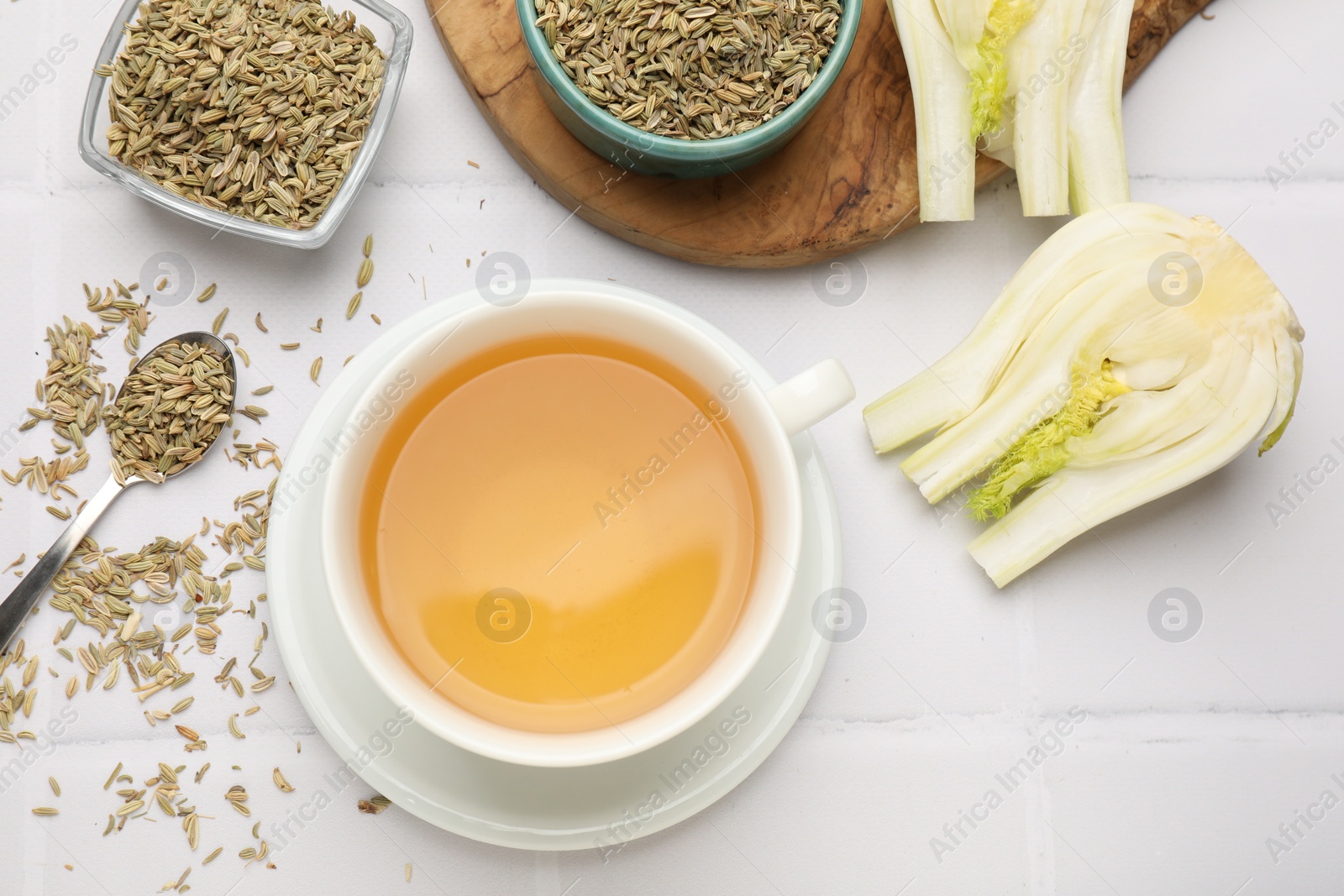 Photo of Fennel tea in cup, seeds and fresh vegetable on white tiled table, flat lay