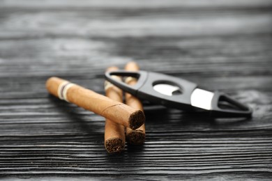 Photo of Cigars and guillotine cutter on black wooden table, closeup