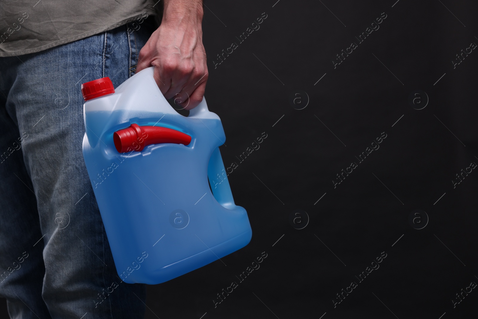 Photo of Man holding canister with blue liquid on black background, closeup. Space for text