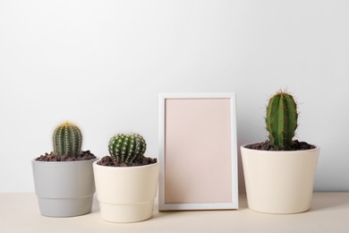 Photo of Different cacti in pots and empty frame on beige table