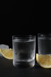 Photo of Shot glasses of vodka with lemon slices and ice on black background