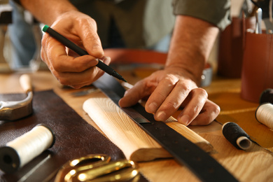 Photo of Man marking holes on leather belt in workshop, closeup