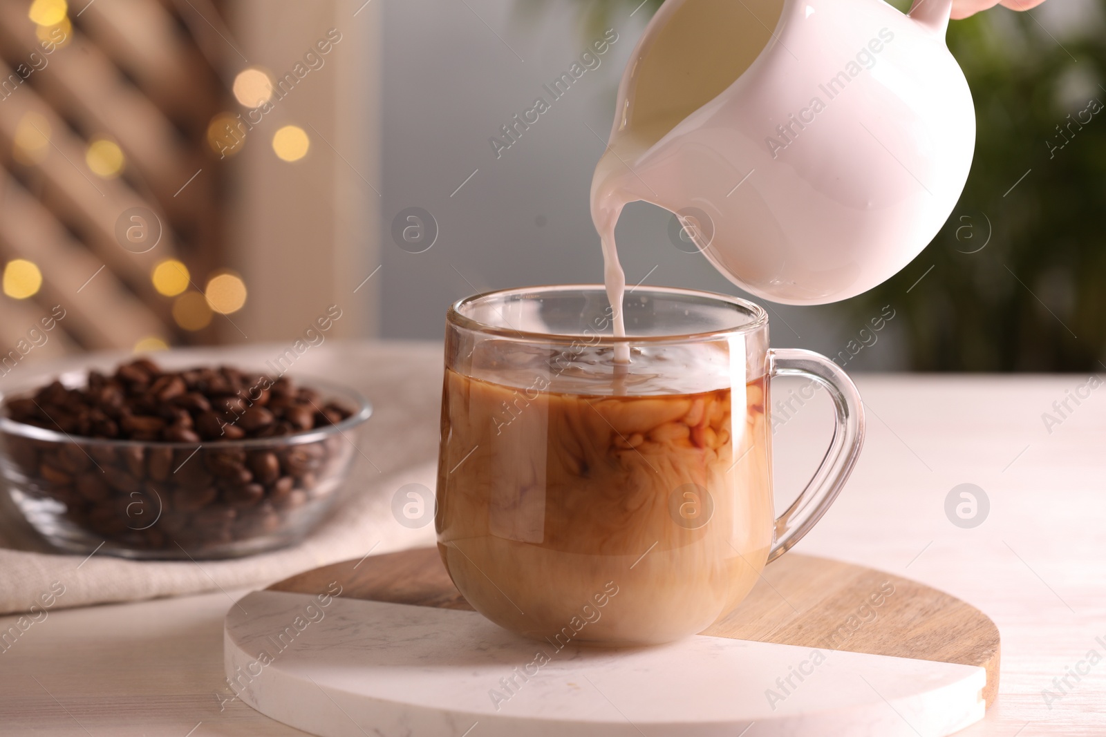 Photo of Woman pouring milk into cup with aromatic coffee at white wooden table, closeup