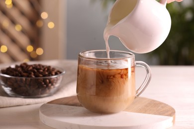 Photo of Woman pouring milk into cup with aromatic coffee at white wooden table, closeup