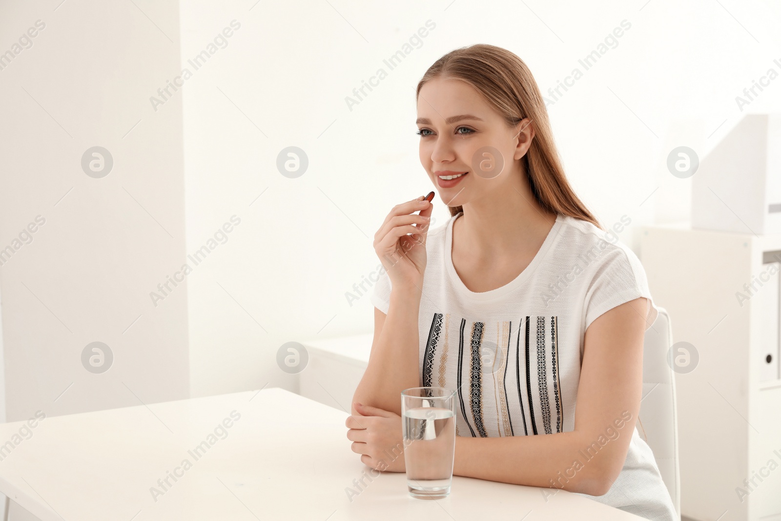 Photo of Young woman taking vitamin capsule at table indoors. Space for text