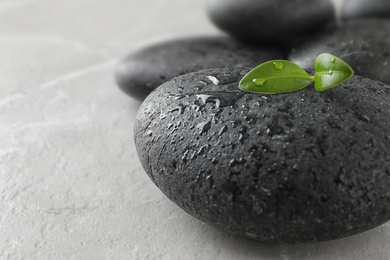 Photo of Spa stones and green leaves with water drops on grey table, space for text