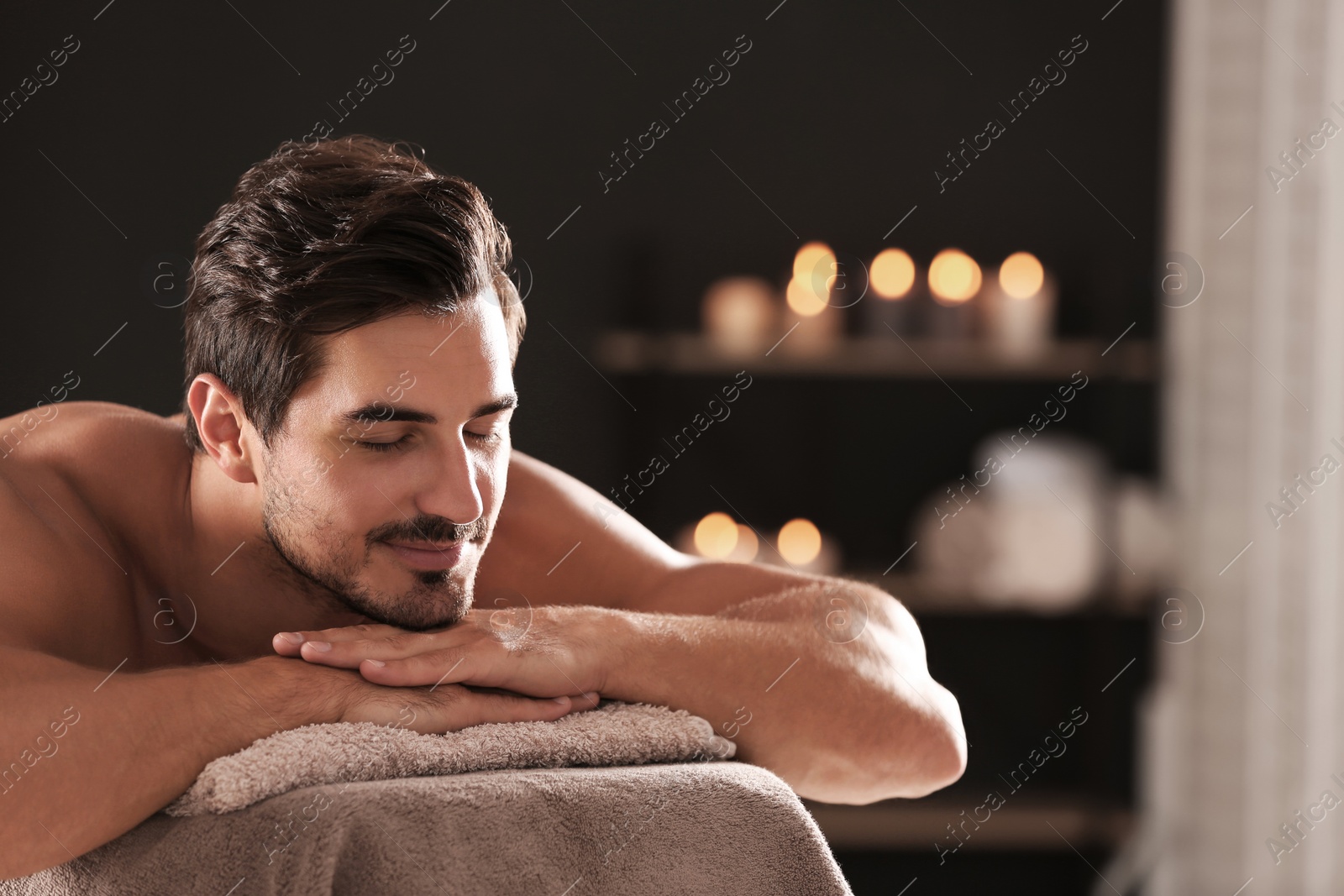 Photo of Handsome young man relaxing on massage table in spa salon, space for text