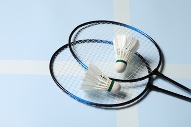 Photo of Feather badminton shuttlecocks and rackets on light blue background, closeup. Space for text