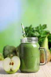 Mason jar of fresh green smoothie and ingredients on wooden table