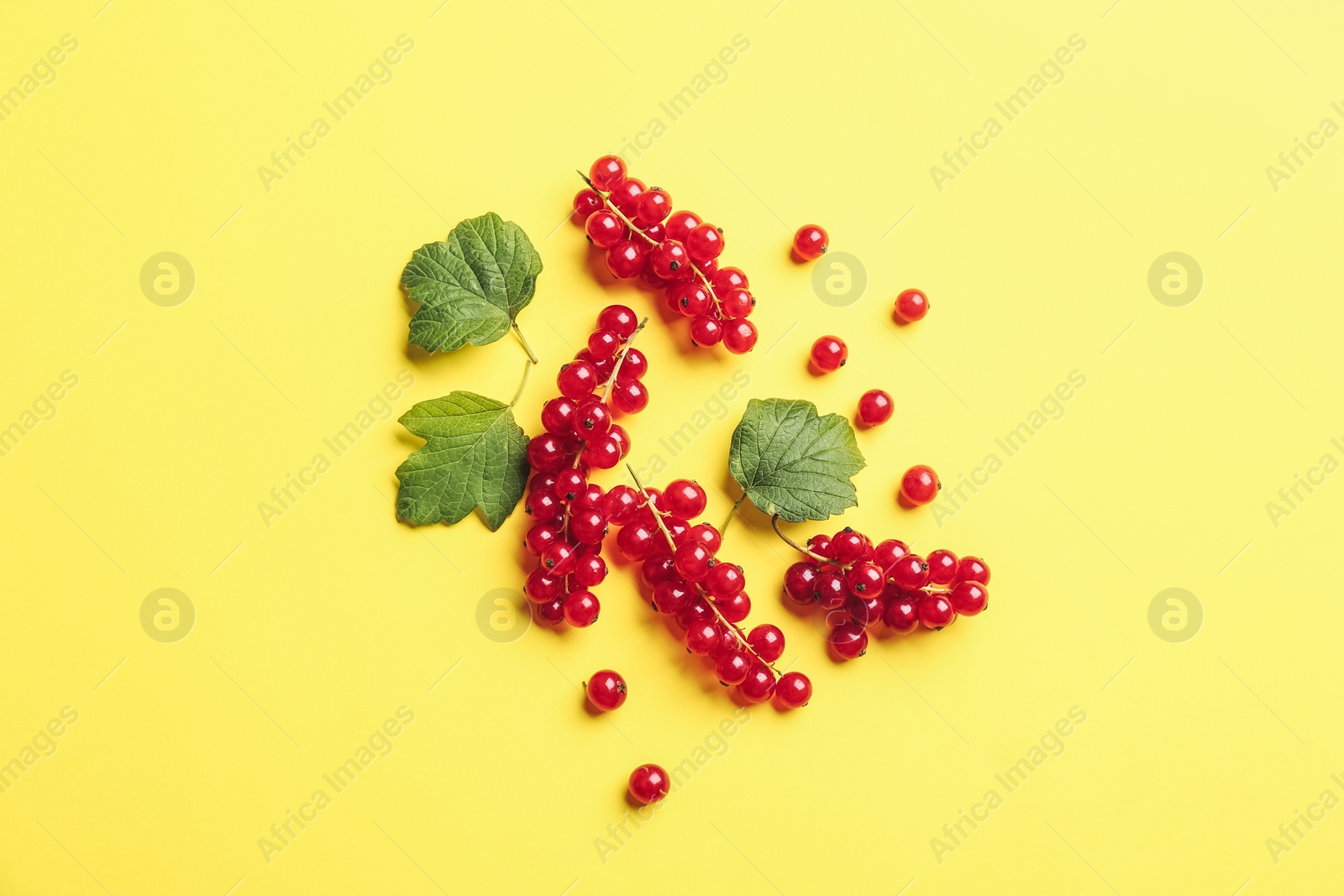 Photo of Delicious red currants and leaves on yellow background, flat lay