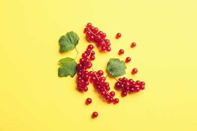 Delicious red currants and leaves on yellow background, flat lay