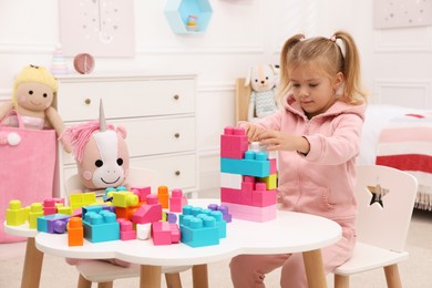 Photo of Cute little girl playing with colorful building blocks at table in room