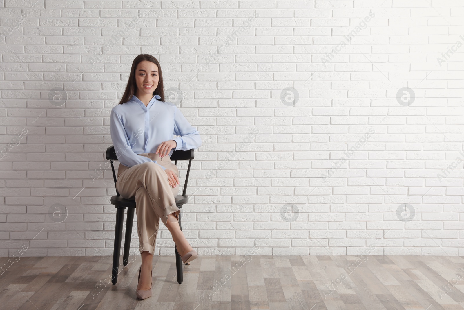 Photo of Young businesswoman sitting in office chair near white brick wall indoors, space for text