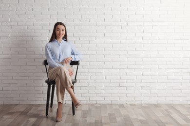 Photo of Young businesswoman sitting in office chair near white brick wall indoors, space for text