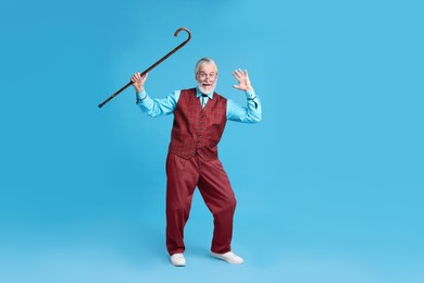 Emotional senior man with walking cane on light blue background