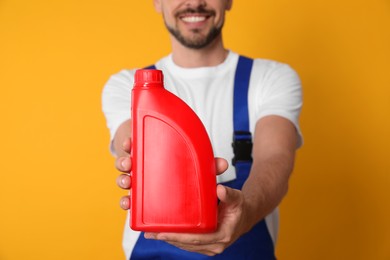 Man showing red container of motor oil on orange background, closeup