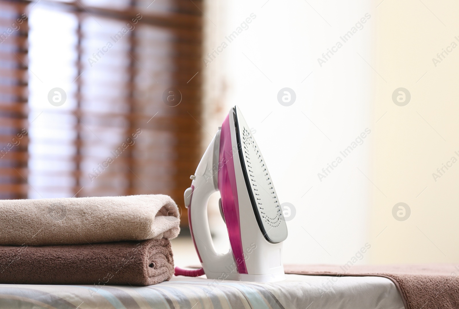 Photo of Modern iron and towels on board in room. Space for text