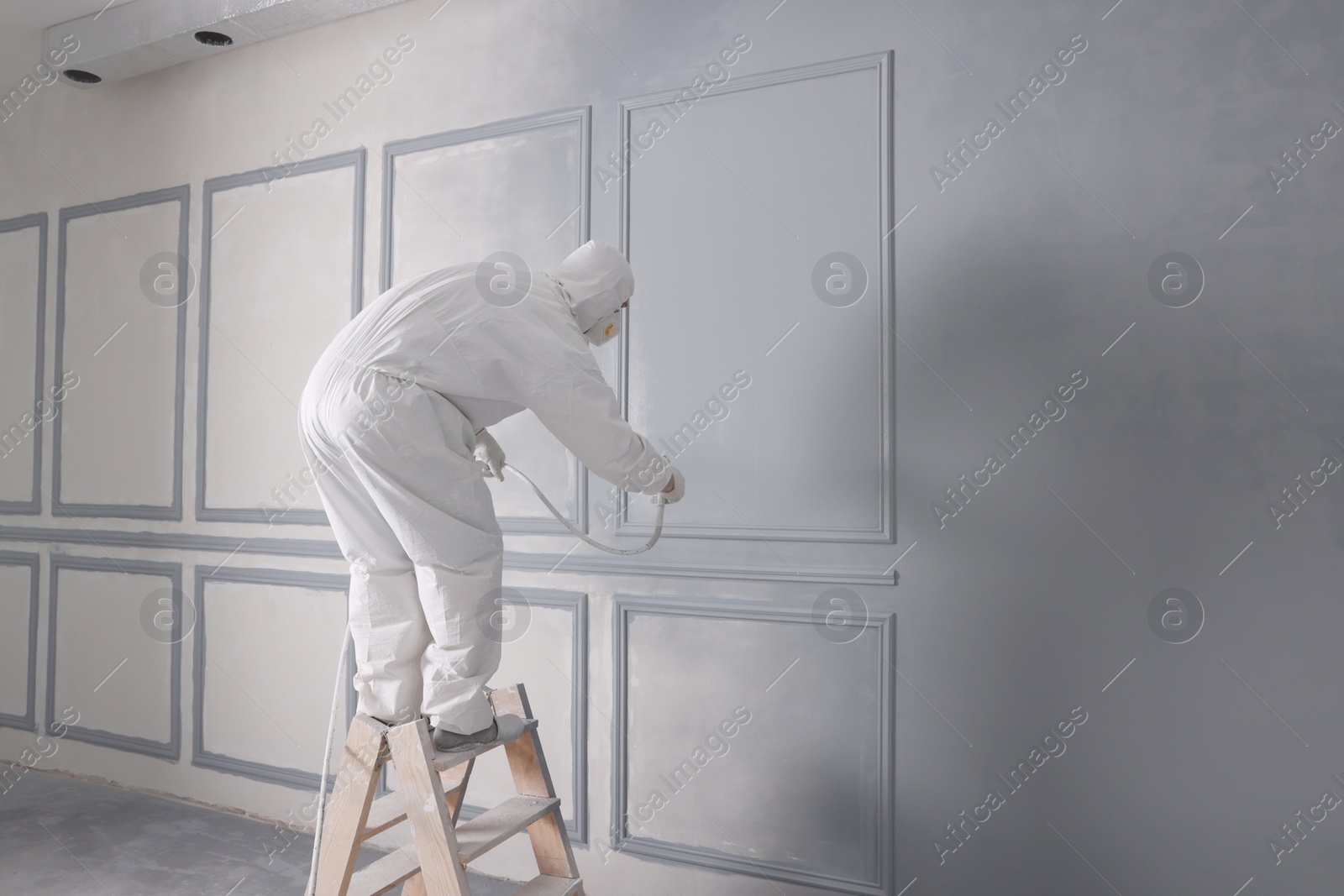 Photo of Decorator dyeing wall in grey color with spray paint