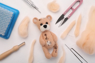 Photo of Felted bear, wool and different tools on white table, flat lay