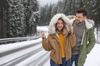 Couple walking near snowy forest, space for text. Winter vacation