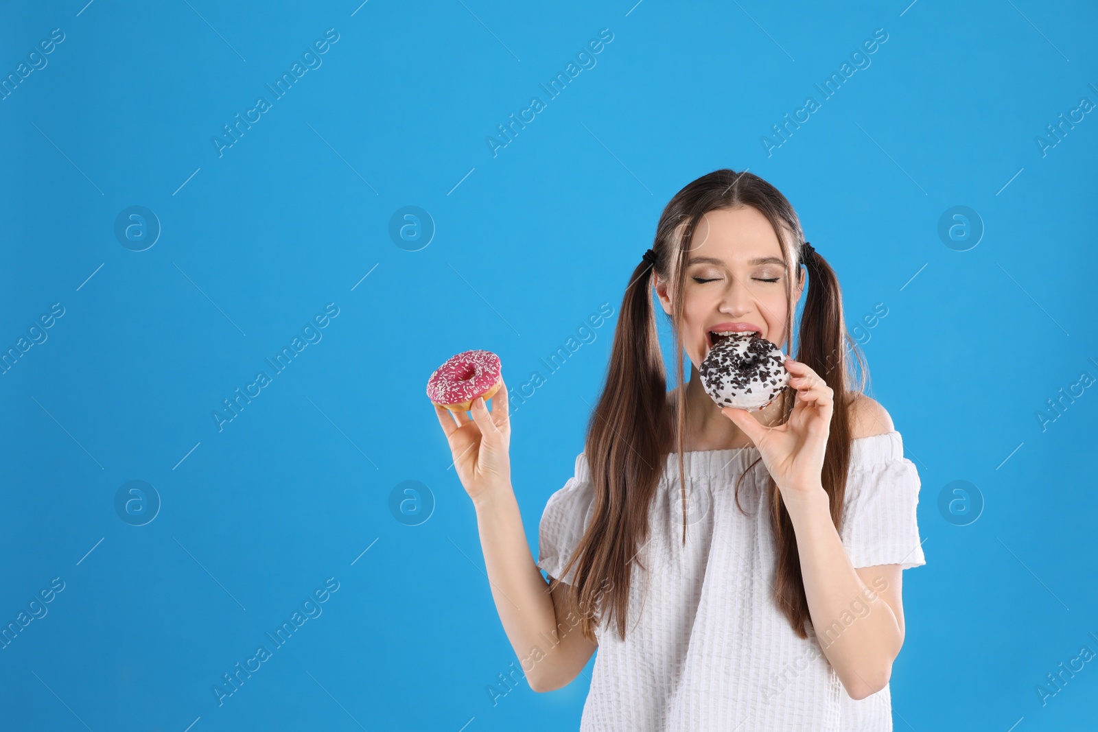 Photo of Beautiful young woman with donuts on light blue background. Space for text