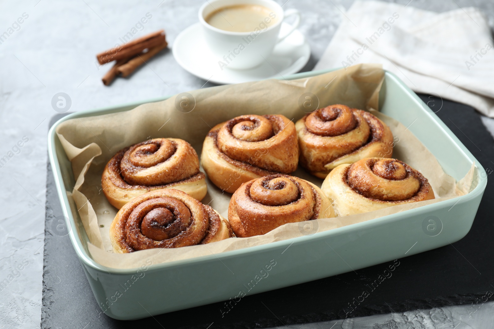 Photo of Baking dish with tasty cinnamon rolls on grey textured table, closeup