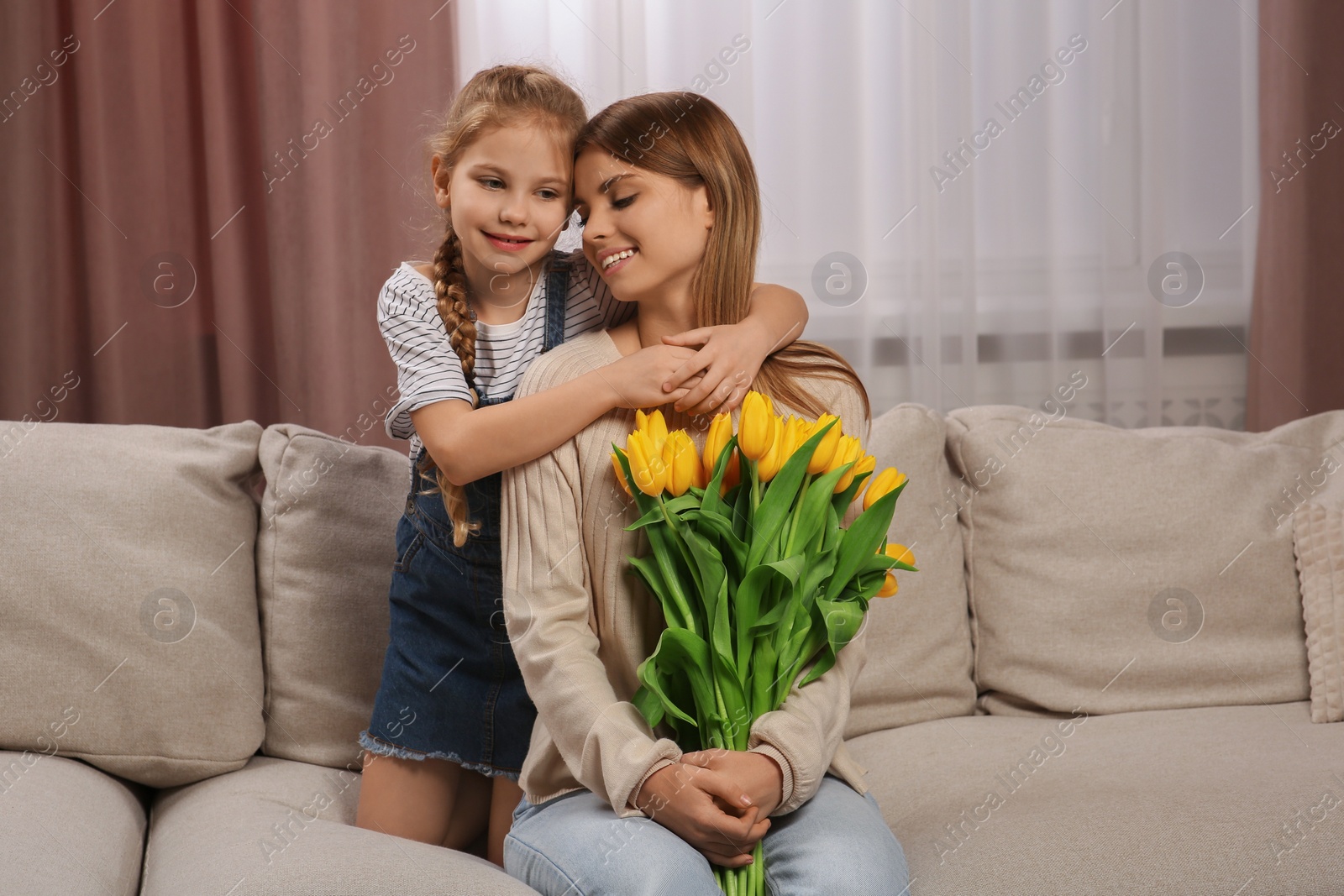 Photo of Little daughter congratulating mom with bouquet of yellow tulips at home. Happy Mother's Day