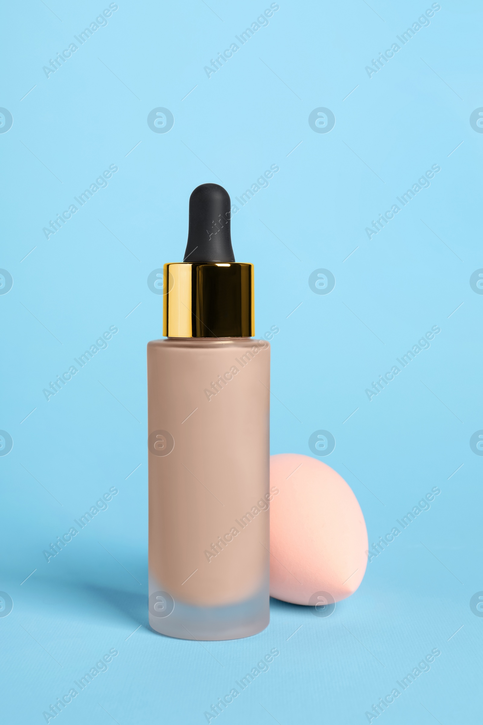 Photo of Bottle of skin foundation and sponge on light blue background. Makeup product