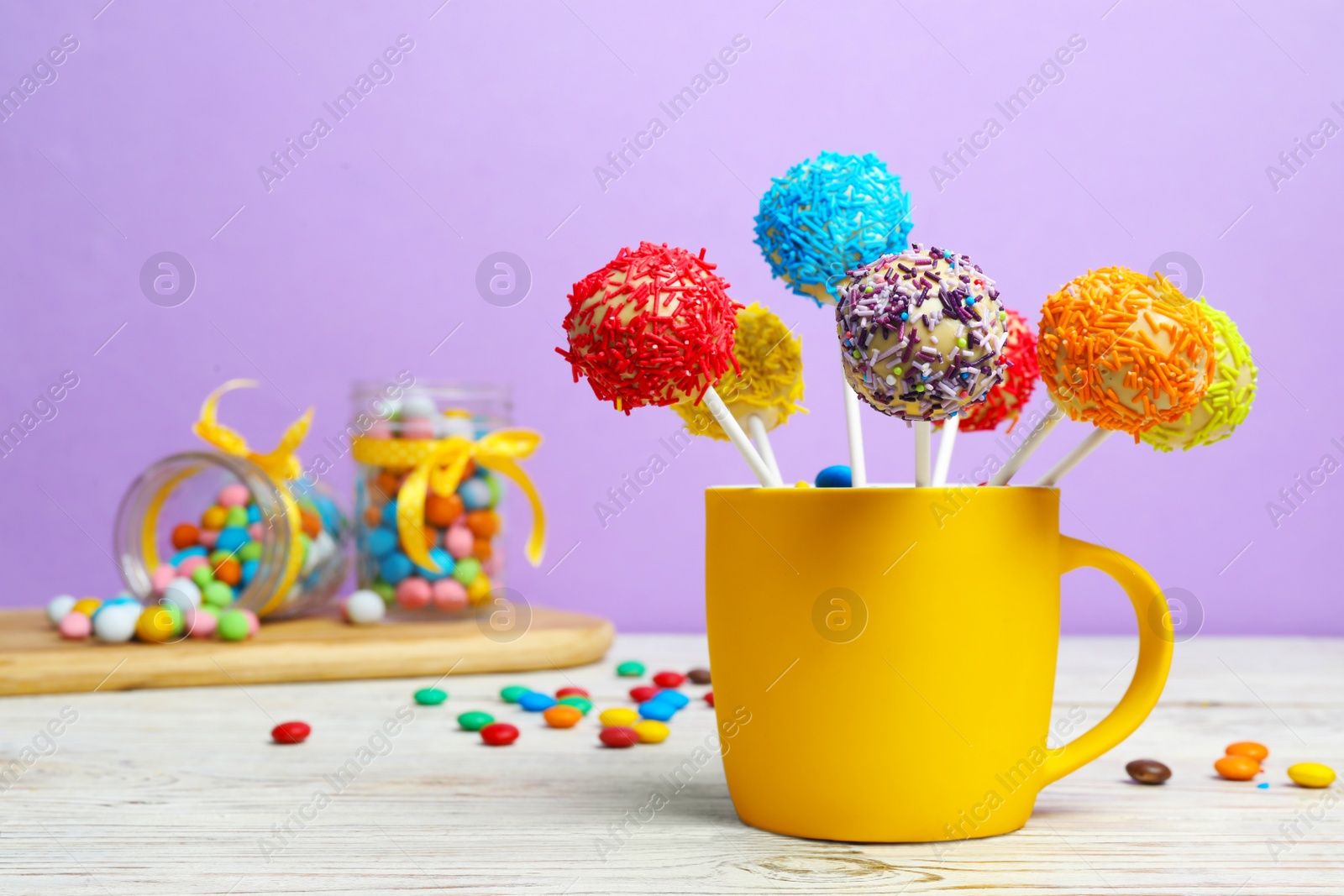 Photo of Cup with tasty cake pops on table against lilac background, space for text