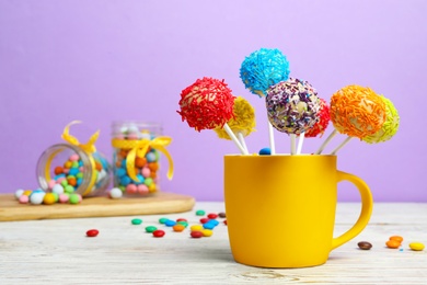 Photo of Cup with tasty cake pops on table against lilac background, space for text