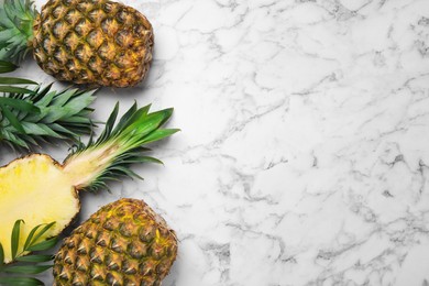 Whole and cut ripe pineapples on white marble table, flat lay. Space for text