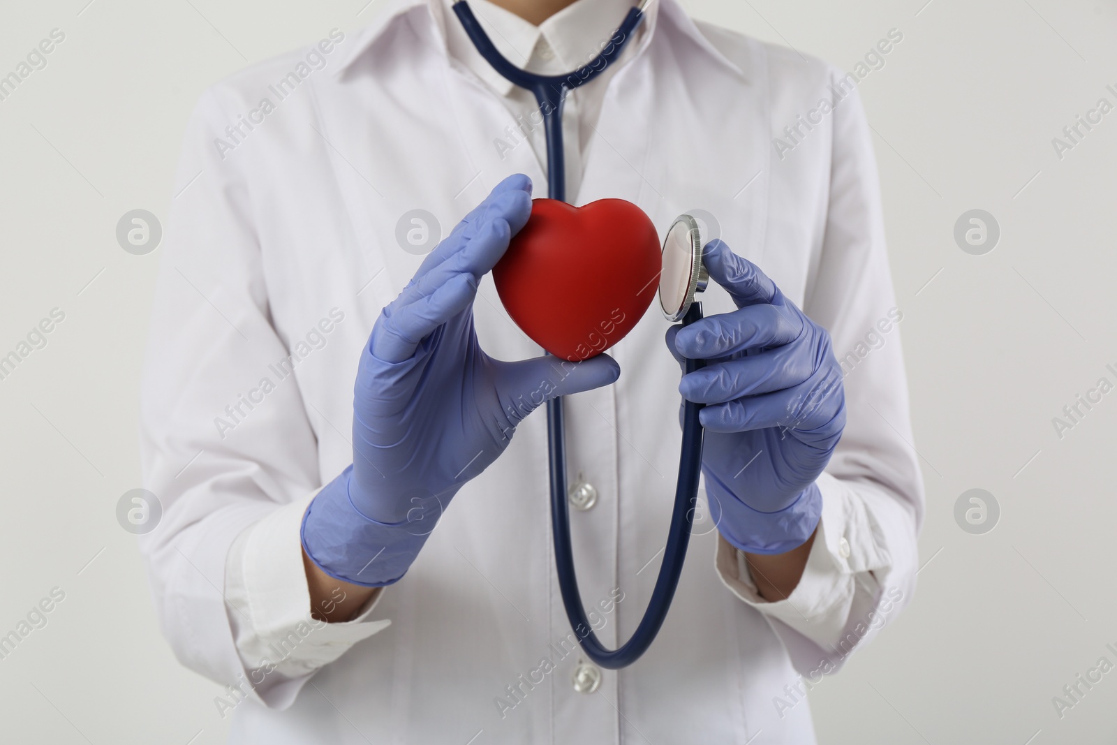 Photo of Doctor with stethoscope and red heart on white background, closeup. Cardiology concept