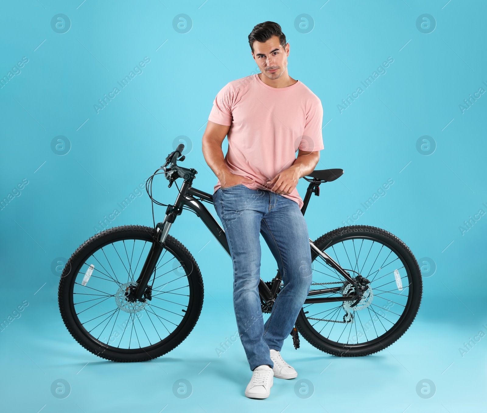 Photo of Handsome young man with modern bicycle on light blue background