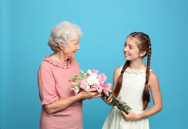Cute girl congratulating her grandmother on light blue background
