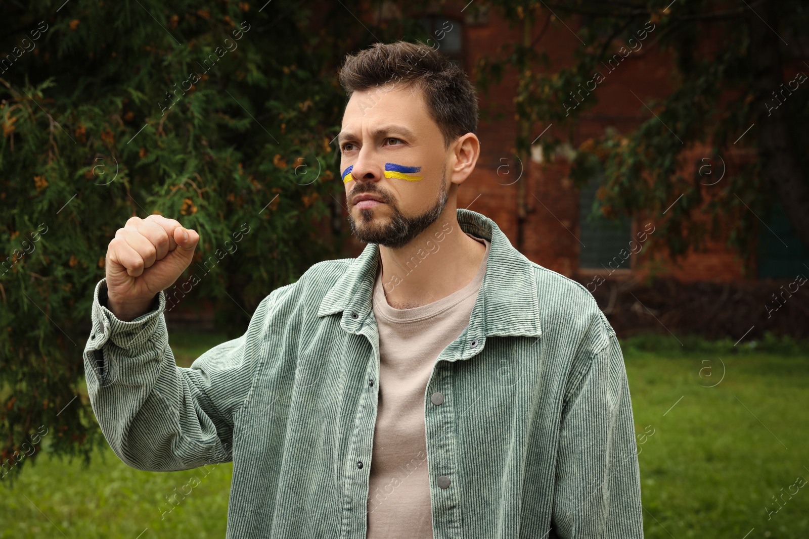 Photo of Angry man with drawings of Ukrainian flag on face outdoors