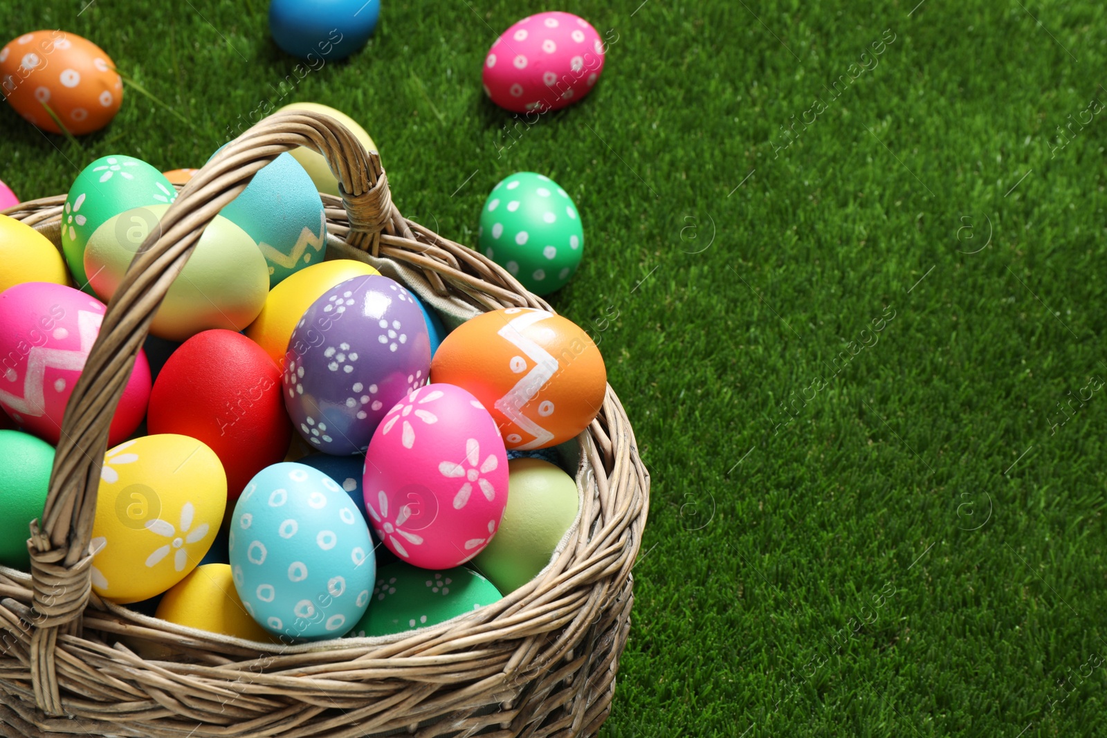 Photo of Colorful Easter eggs in basket on green grass, closeup. Space for text