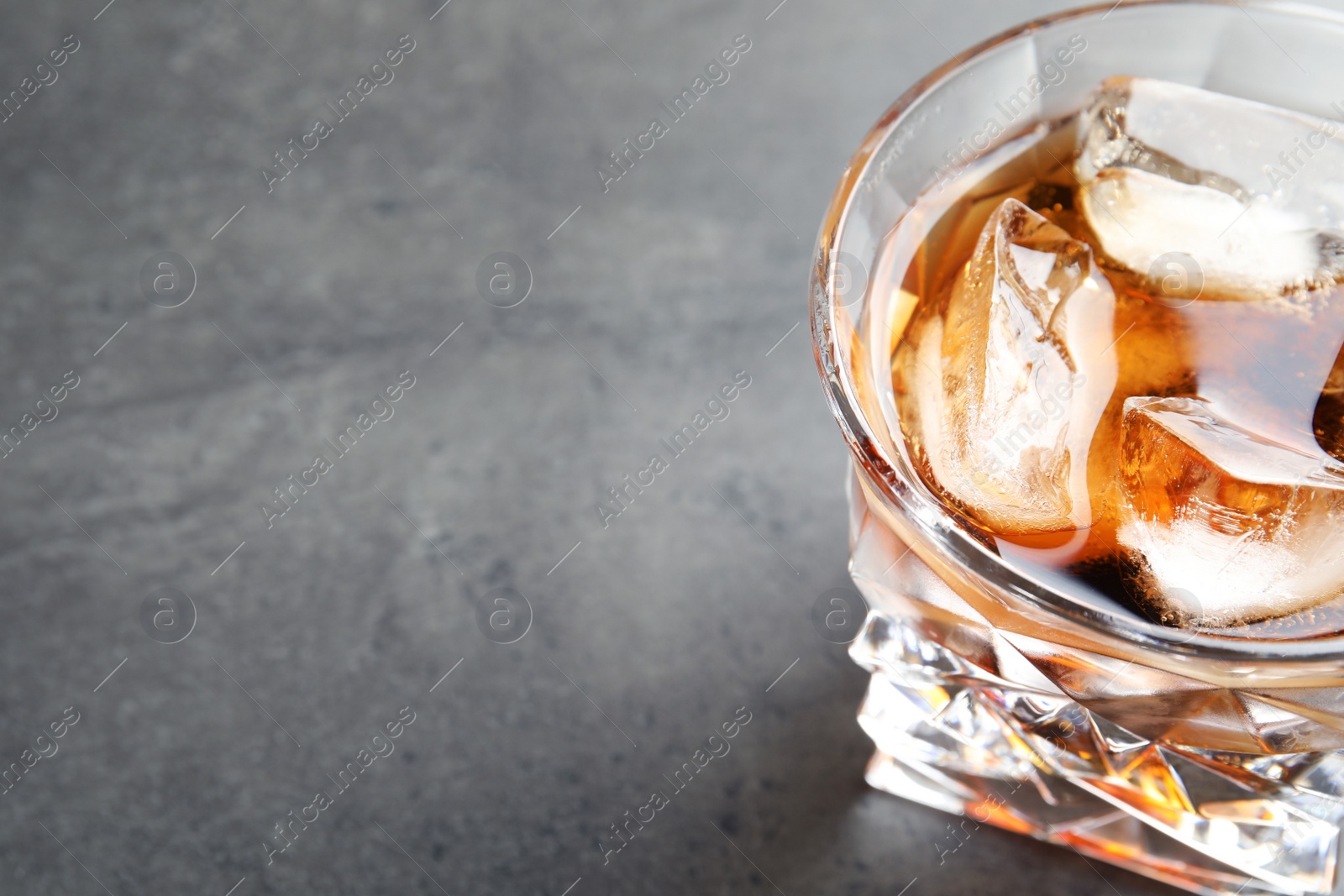 Photo of Glass of whiskey with ice cubes on grey table. Space for text