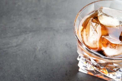 Glass of whiskey with ice cubes on grey table. Space for text