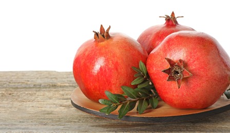 Photo of Fresh pomegranates and green leaves on wooden table against white background, space for text