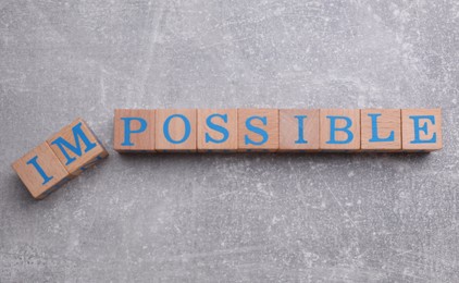 Photo of Motivation concept. Changing word from Impossible into Possible by removing wooden cubes on light grey table, flat lay