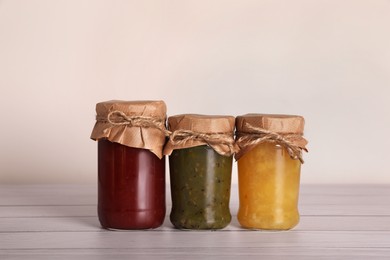 Jars with preserved fruit jams on white wooden table