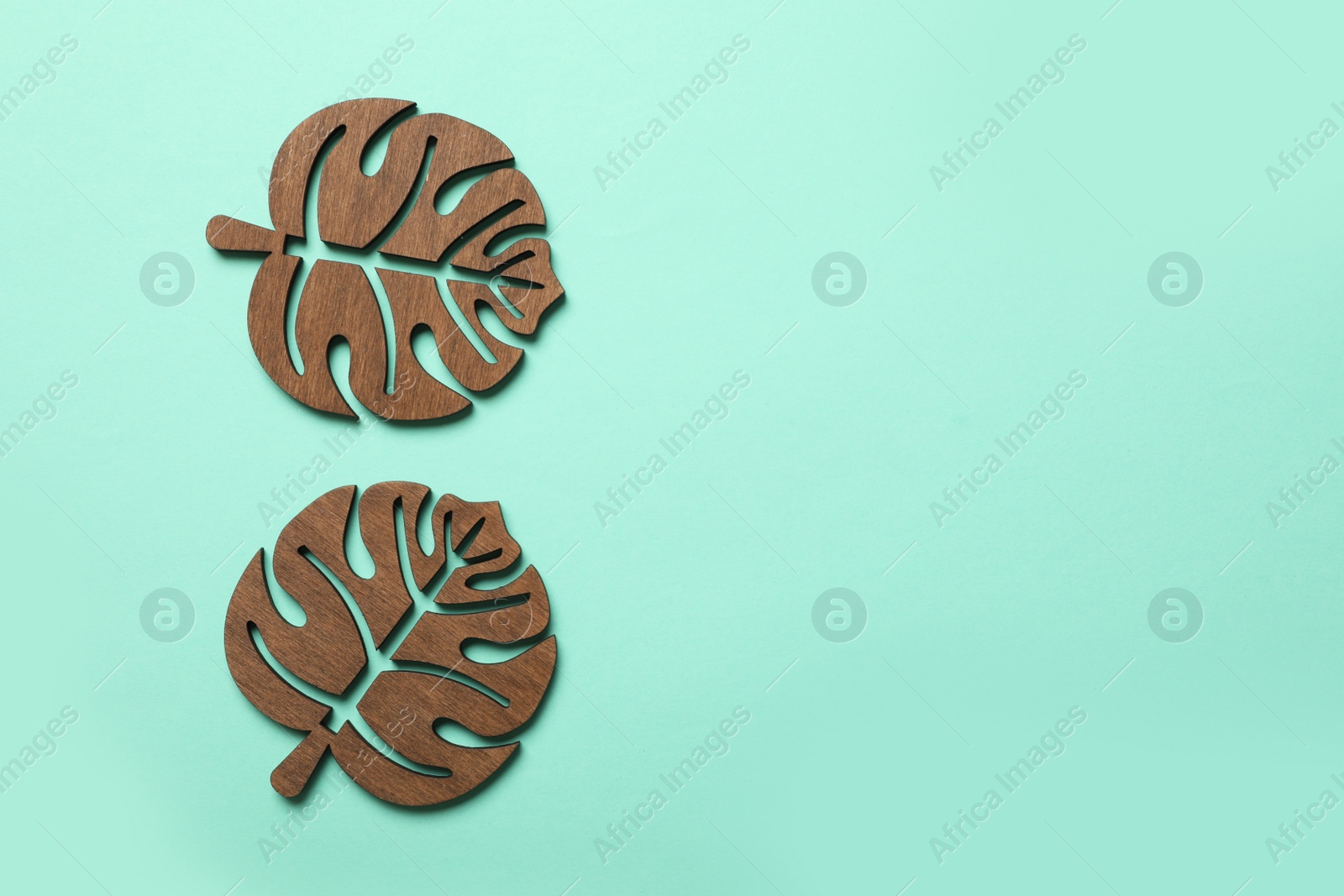 Photo of Leaf shaped wooden cup coasters on turquoise background, flat lay. Space for text
