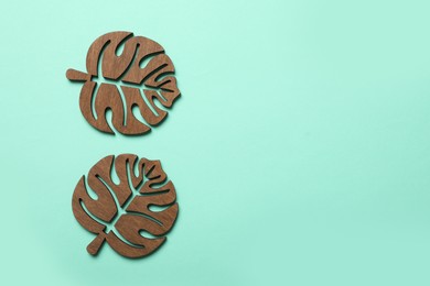 Photo of Leaf shaped wooden cup coasters on turquoise background, flat lay. Space for text