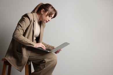 Photo of Young woman with poor posture using laptop while sitting on stool against grey background, space for text