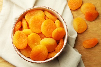 Photo of Tasty apricots with bowl on wooden table, flat lay. Dried fruits