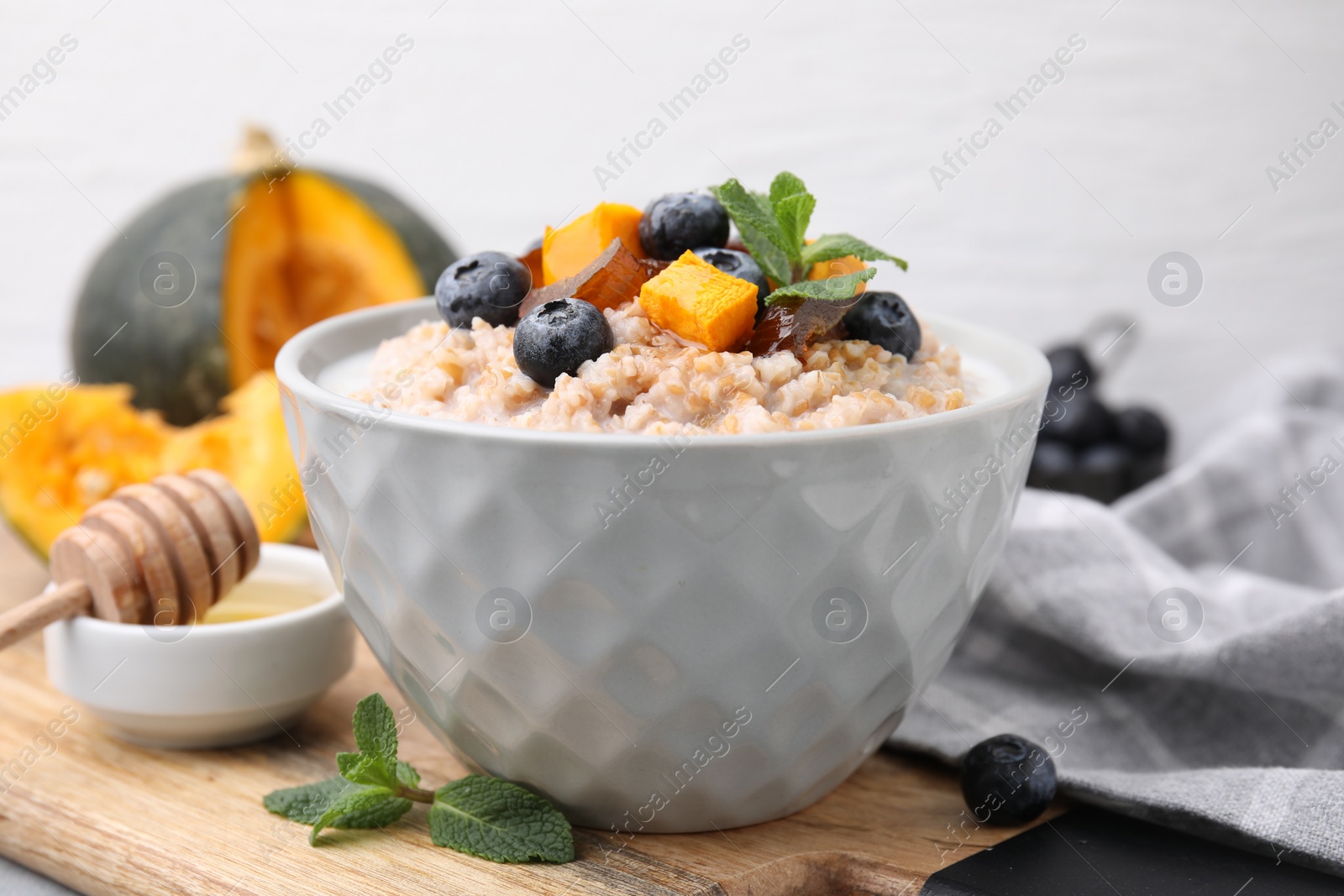 Photo of Tasty wheat porridge with pumpkin, dates and blueberries in bowl on table, closeup