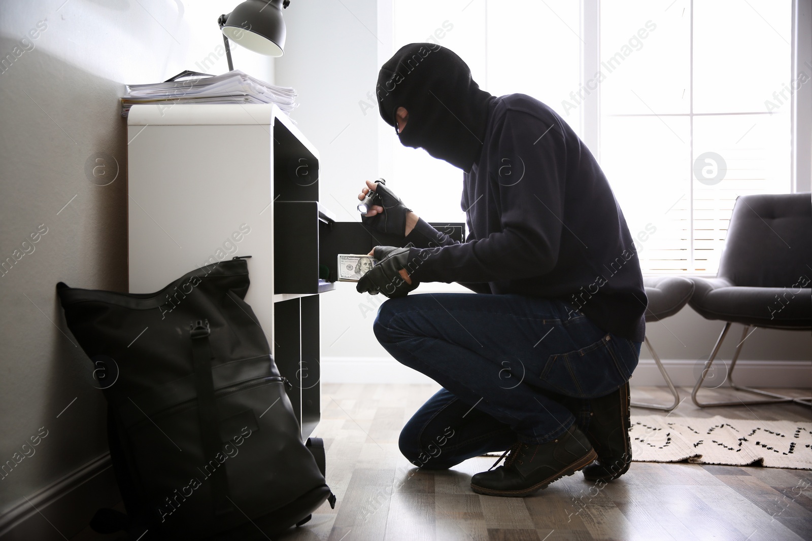 Photo of Thief taking money out of steel safe indoors