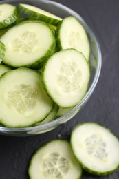Photo of Cut cucumber in glass bowl on dark gray table, above view