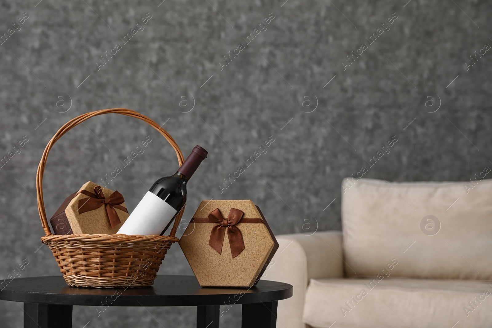 Photo of Wicker basket with bottle of wine and gift boxes on table in room. Space for design